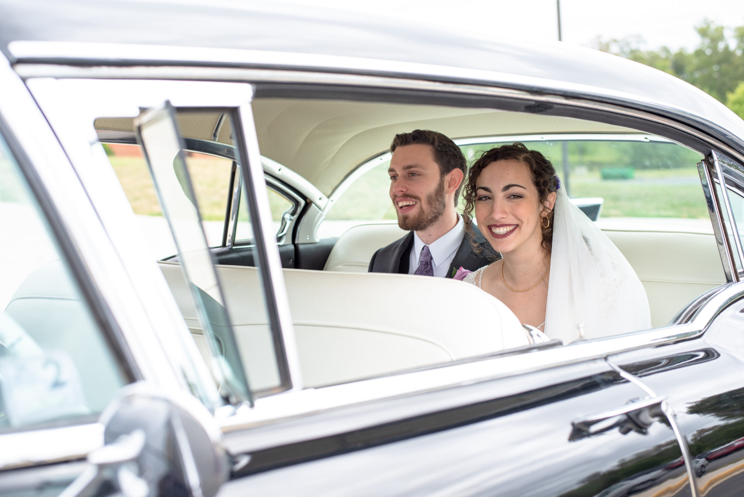 Bride and groom in the back of rented vintage Cadillac car on wedding day