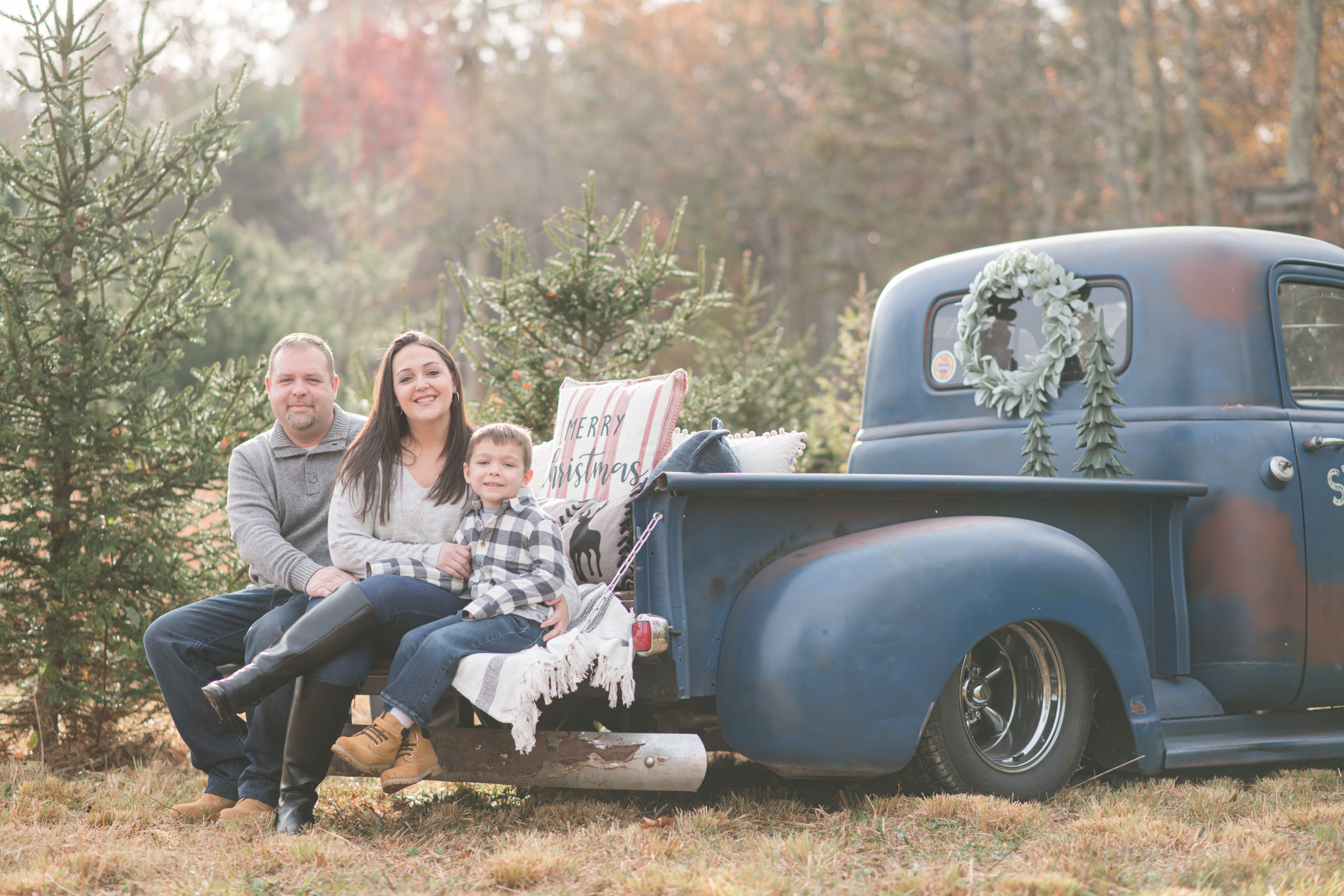 Family of three at christmas tree farm sitting on blue truck
