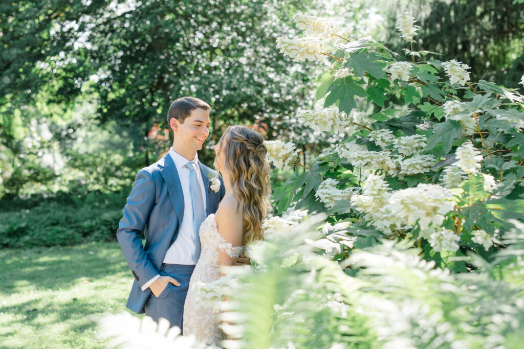 Bride and groom embracing in a lush garden surrounded by white flowering bushes at The Elkridge Furnace Inn.