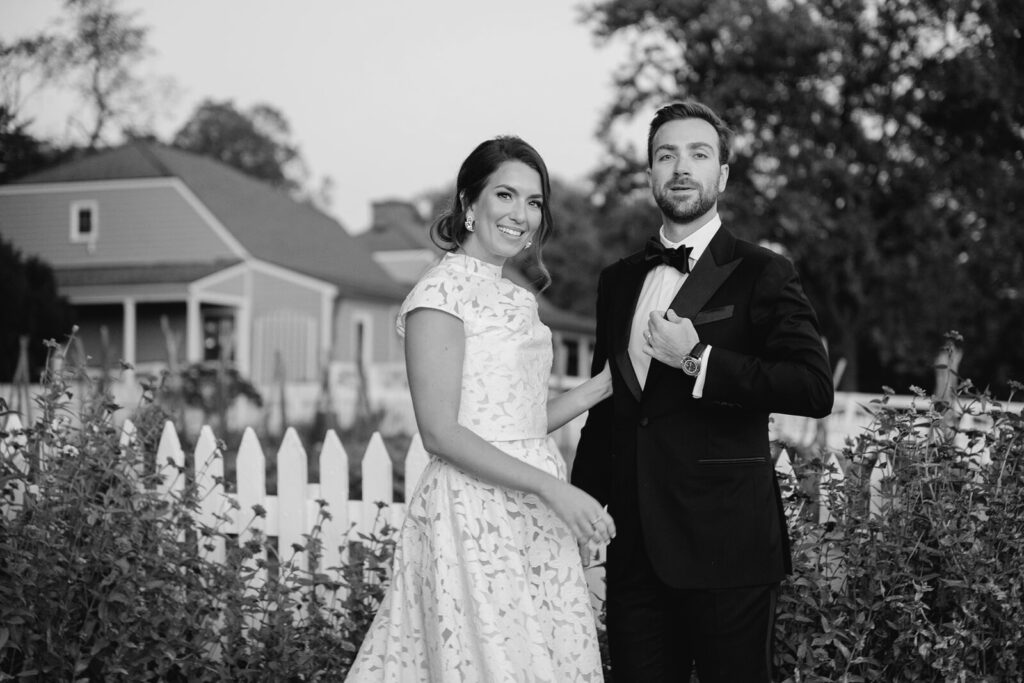 Bride and groom smiling in front of a white picket fence and historic farmhouse at James Monroe’s Highland during their fall wedding, captured by Charlottesville wedding photographer Silverbridge & Co.