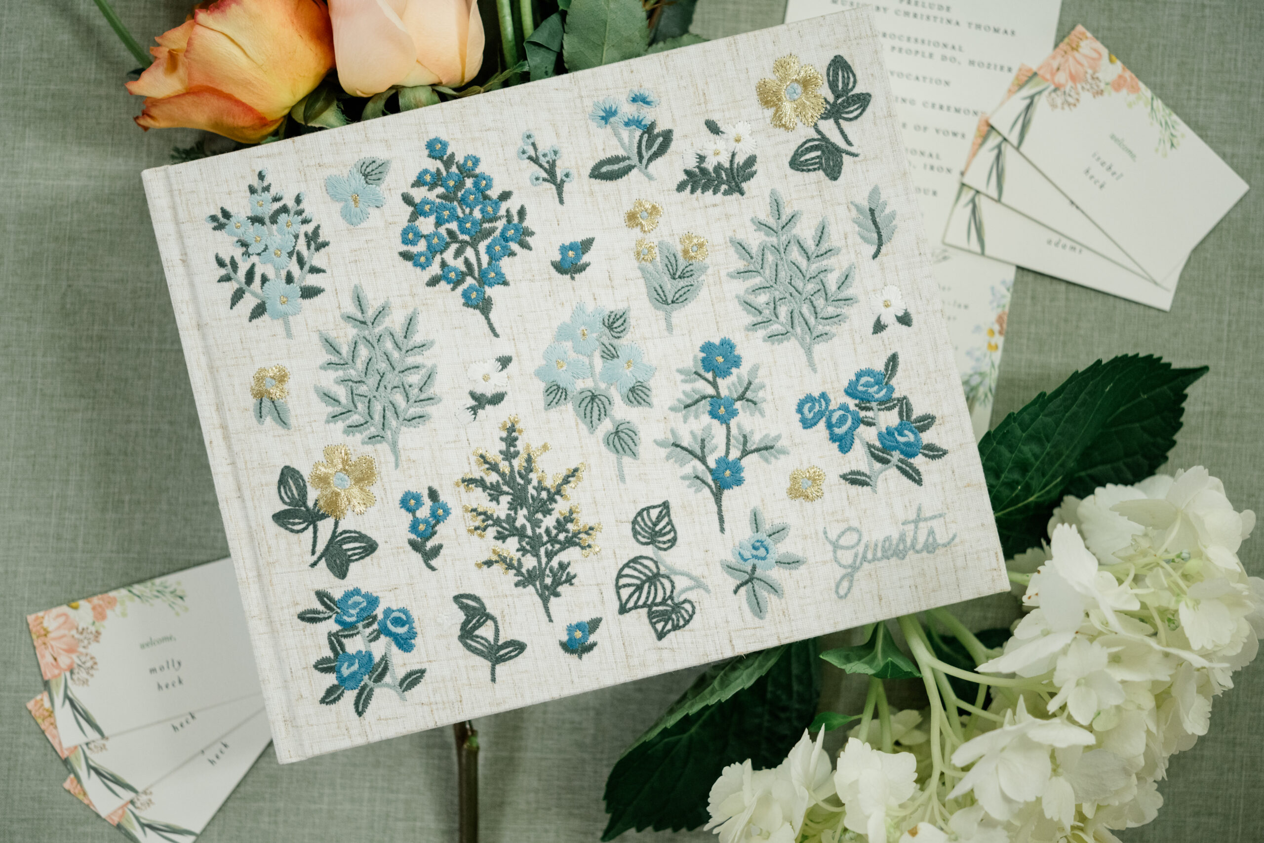 Embroidered floral wedding guestbook with pastel flowers and escort cards nearby.
