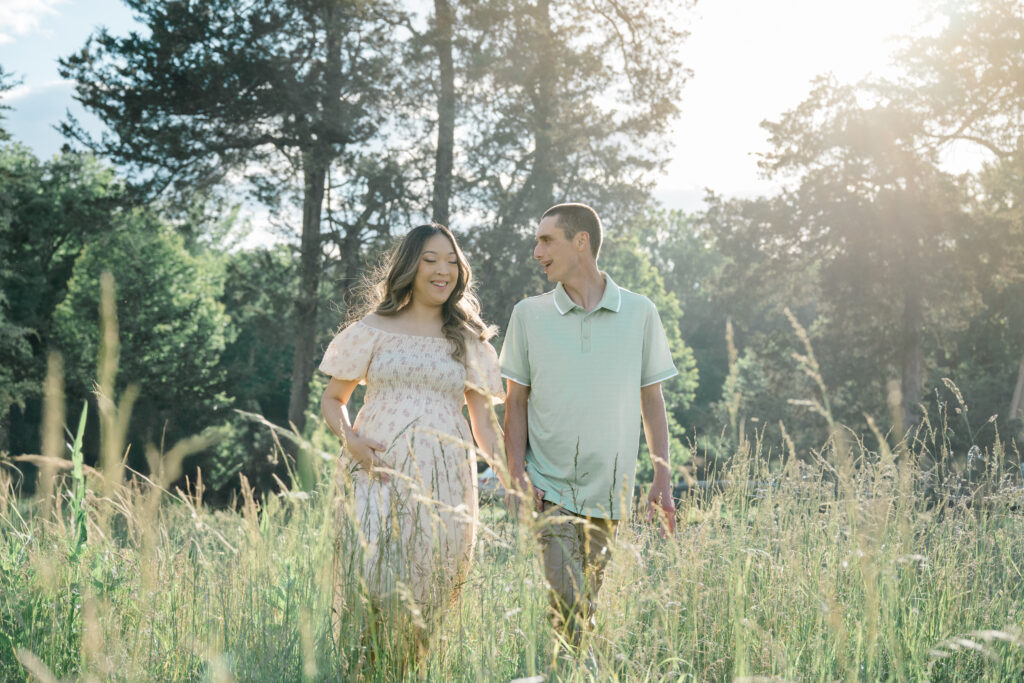 Expecting couple walking hand in hand through a golden field during their golden hour maternity session at Historic Tuckahoe near Richmond, VA.