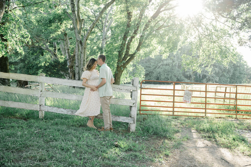 Expecting couple shares a quiet moment near a white fence and pasture at golden hour during a maternity session at Historic Tuckahoe in Virginia.