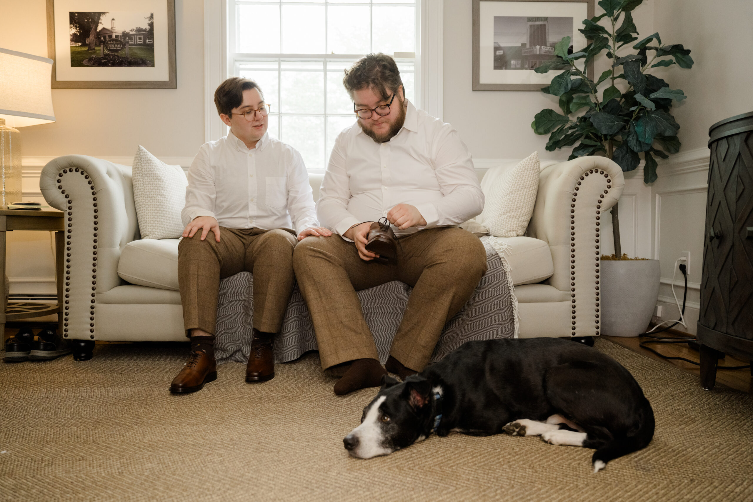 The grooms sitting on a sofa with their dog Marlo lying peacefully on the rug during the wedding morning preparations.