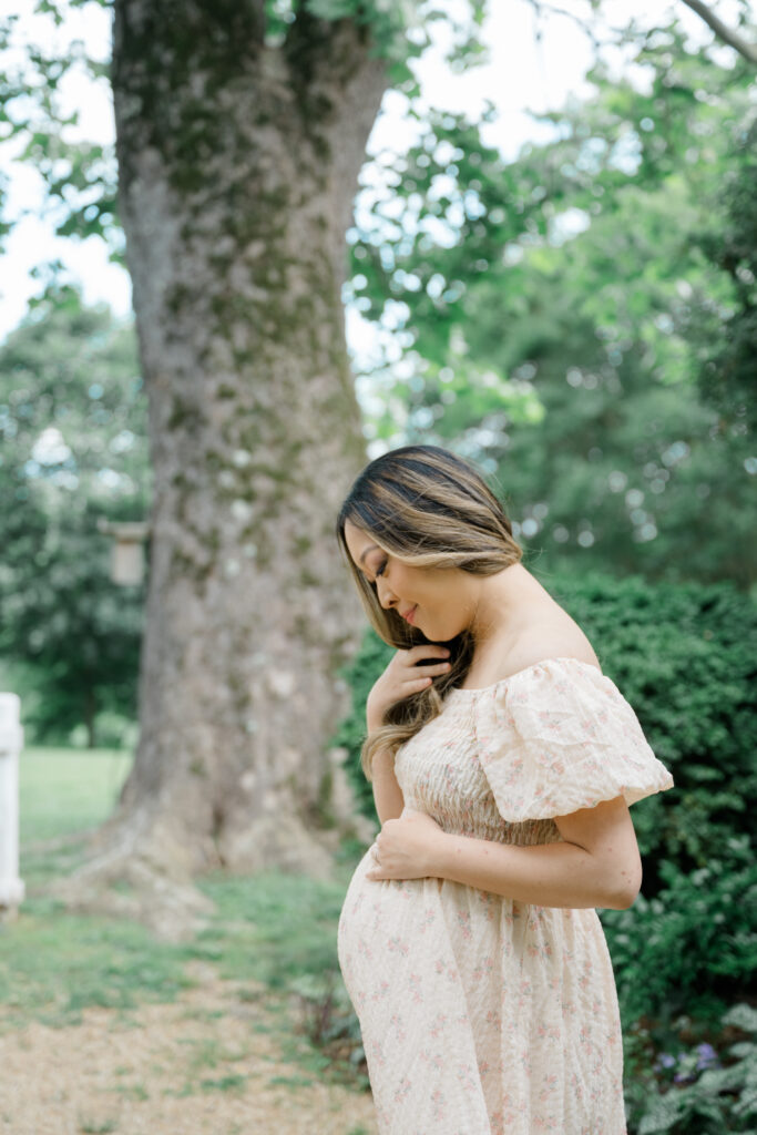 Peaceful maternity portrait of a mother-to-be gently holding her belly beneath a tree at Historic Tuckahoe in Richmond, VA.