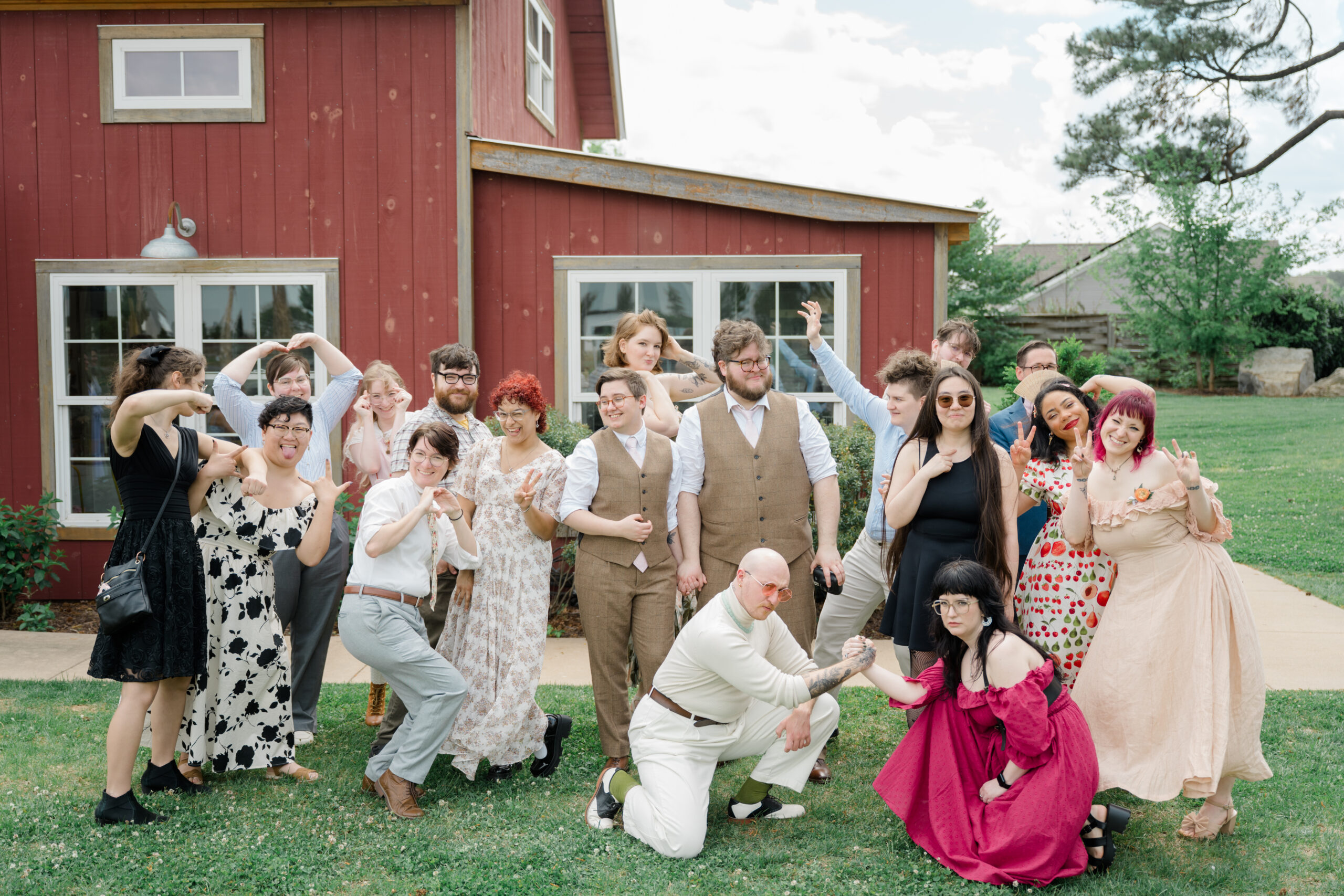 A joyful group photo of LGBTQ+ wedding guests posing playfully on the lawn in front of a red barn at Woodside Farms.