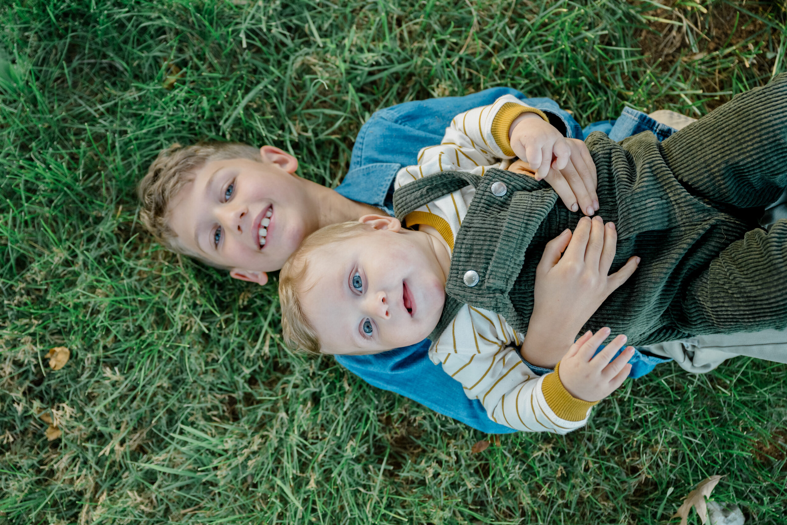 Older brothers lie in the grass with their baby sibling, creating a playful and heartfelt moment during a fall family session in Fluvanna County.