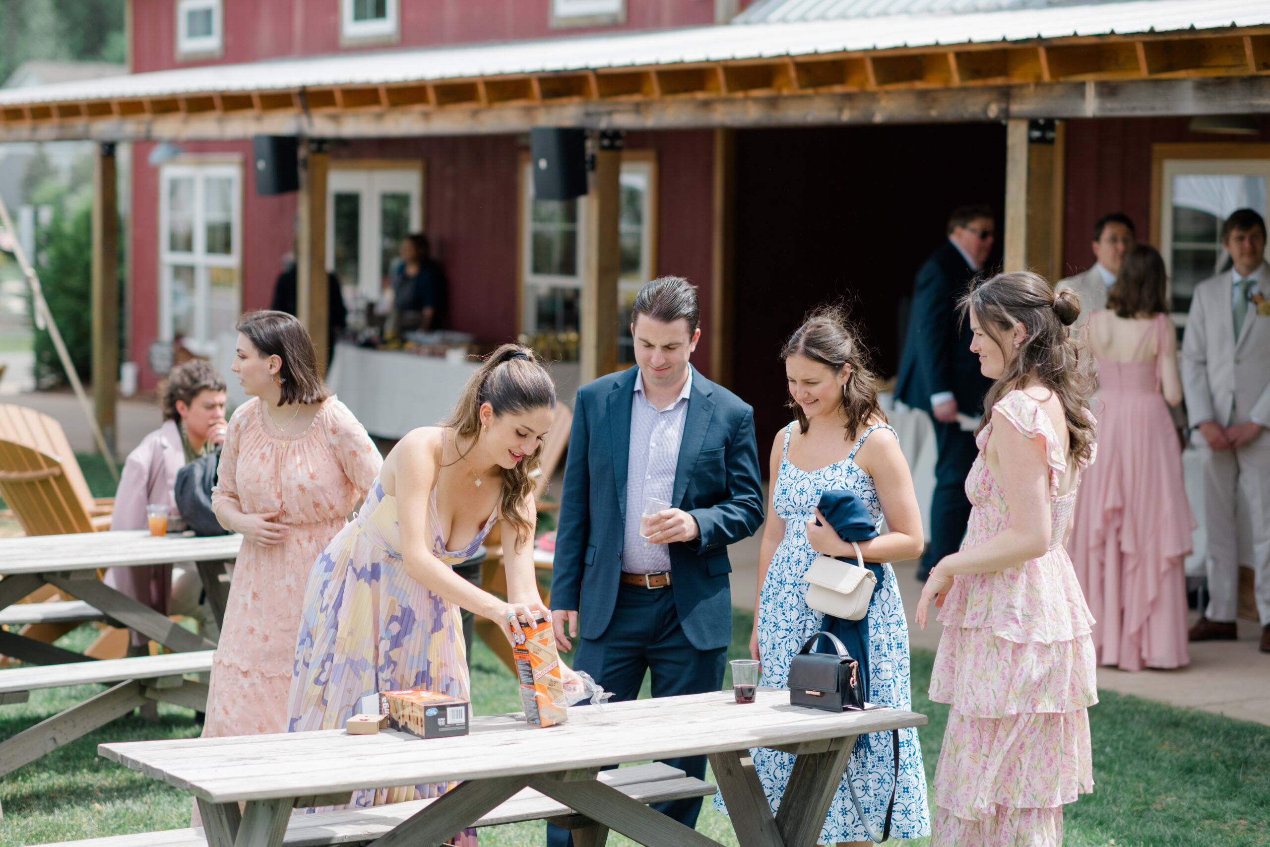 Wedding guests enjoy yard games and drinks outside during a spring brunch reception at Woodside Farms, with a red barn in the background.
