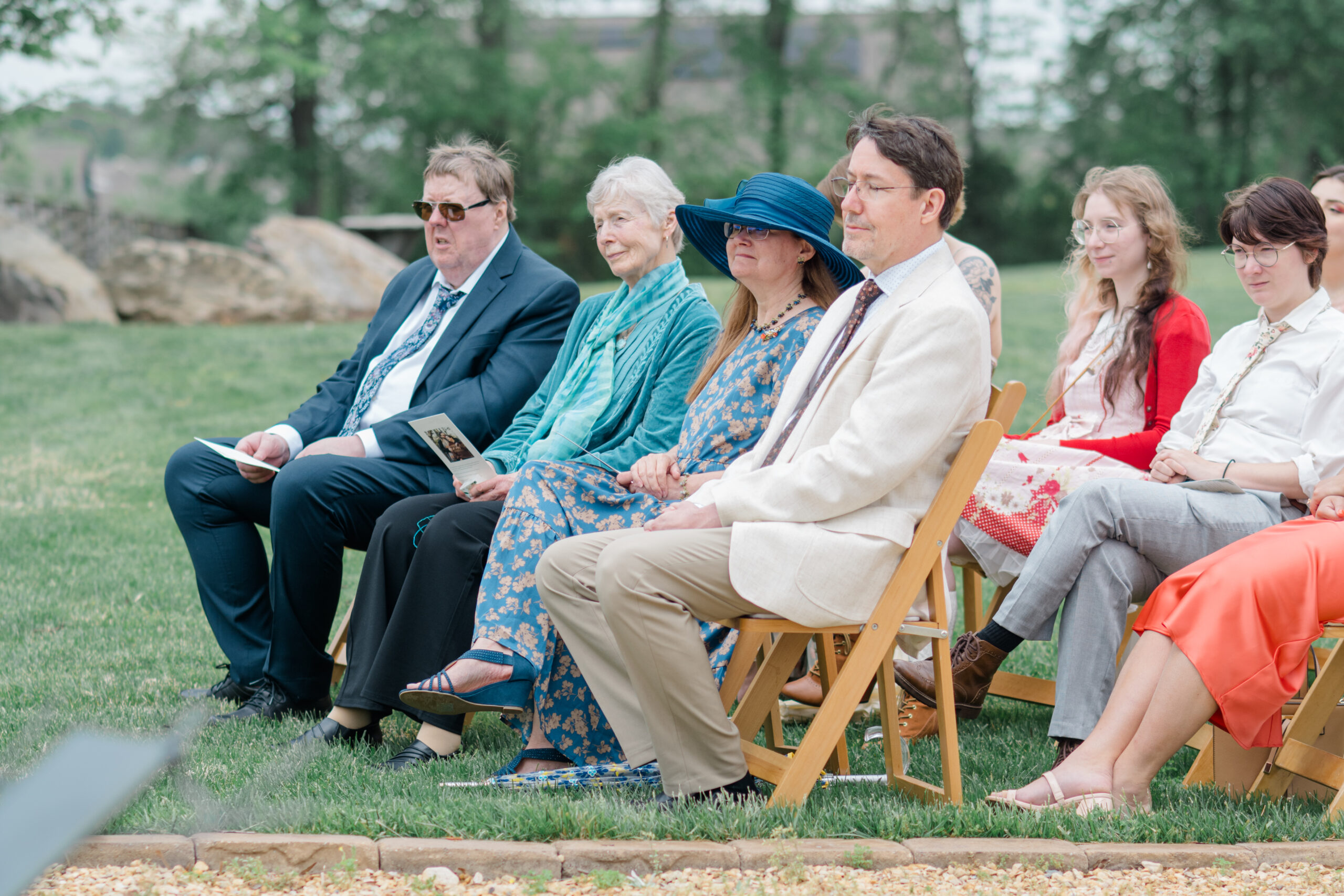 Wedding guests seated outdoors, smiling and waiting for the ceremony to begin.