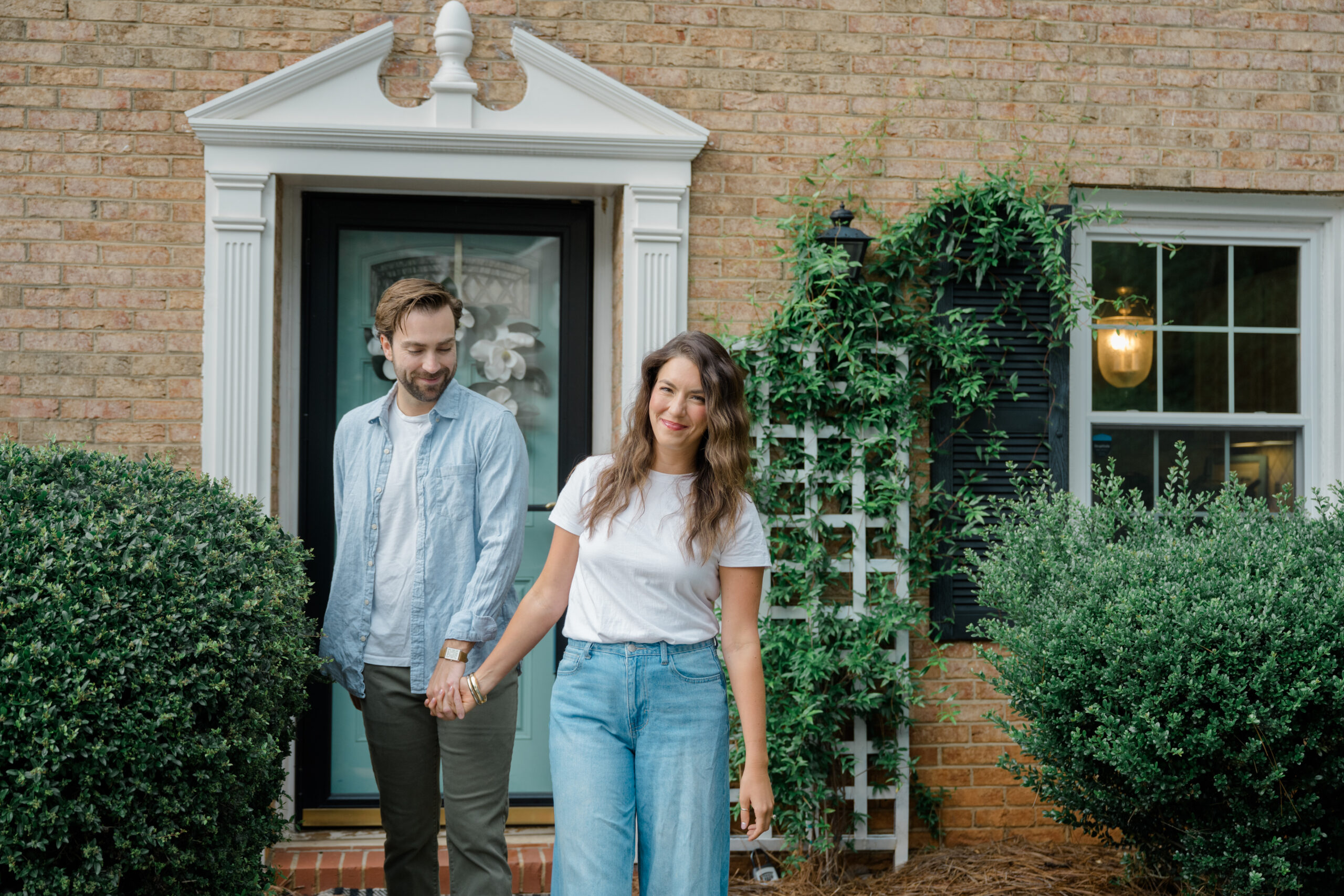 Couple holding hands and smiling outside their first home in Charlotte, North Carolina during an in-home farewell photo session.
