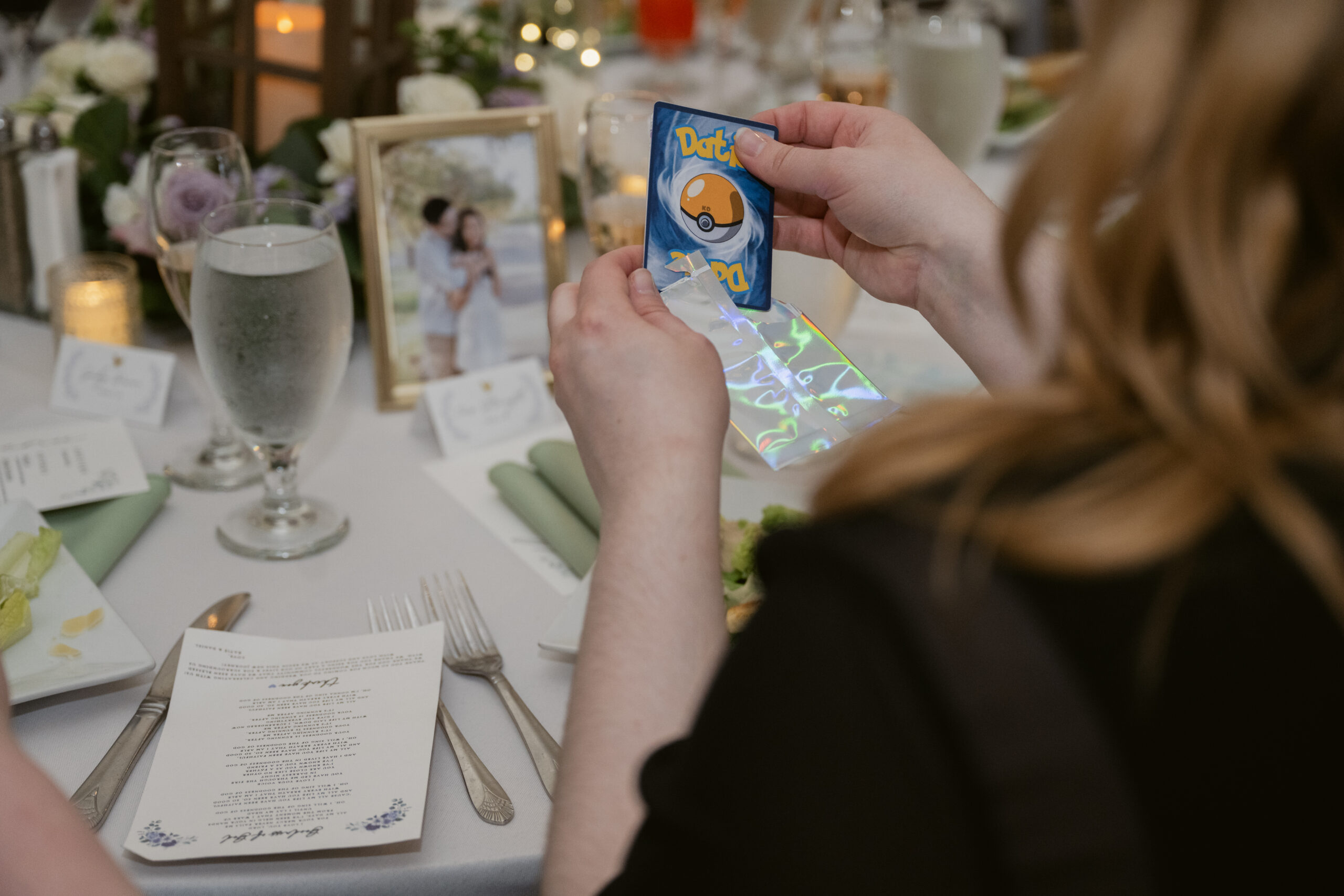 Guest opening a holographic sleeve to reveal a custom Pokémon-style card at their reception table.