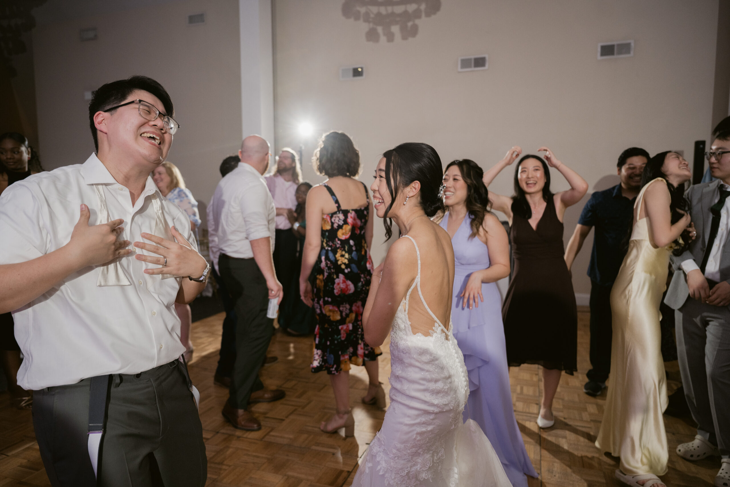 The bride and groom laughing together while dancing, surrounded by guests.