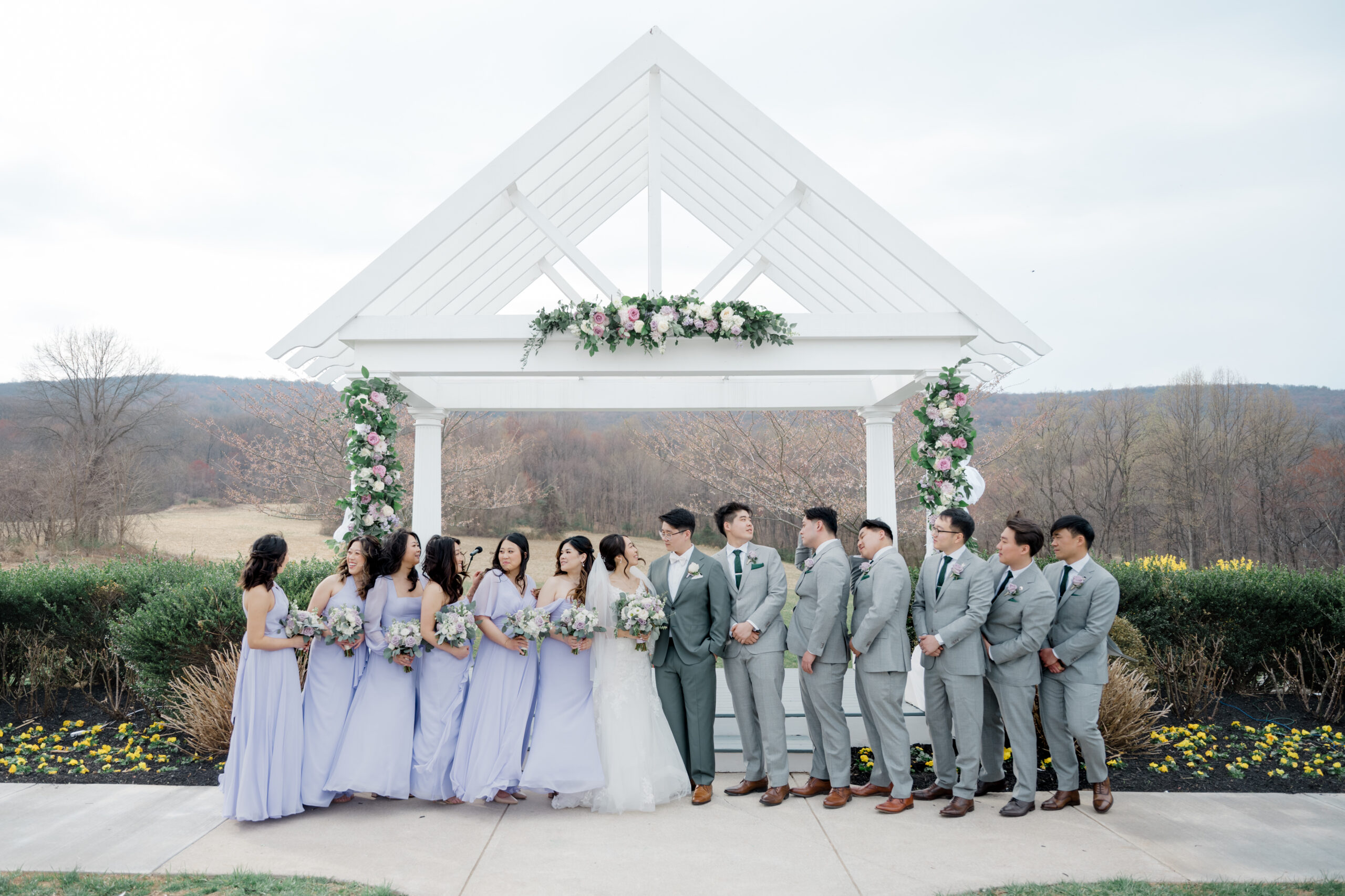 Wedding party standing under a floral-decorated arbor with mountain views in the background.