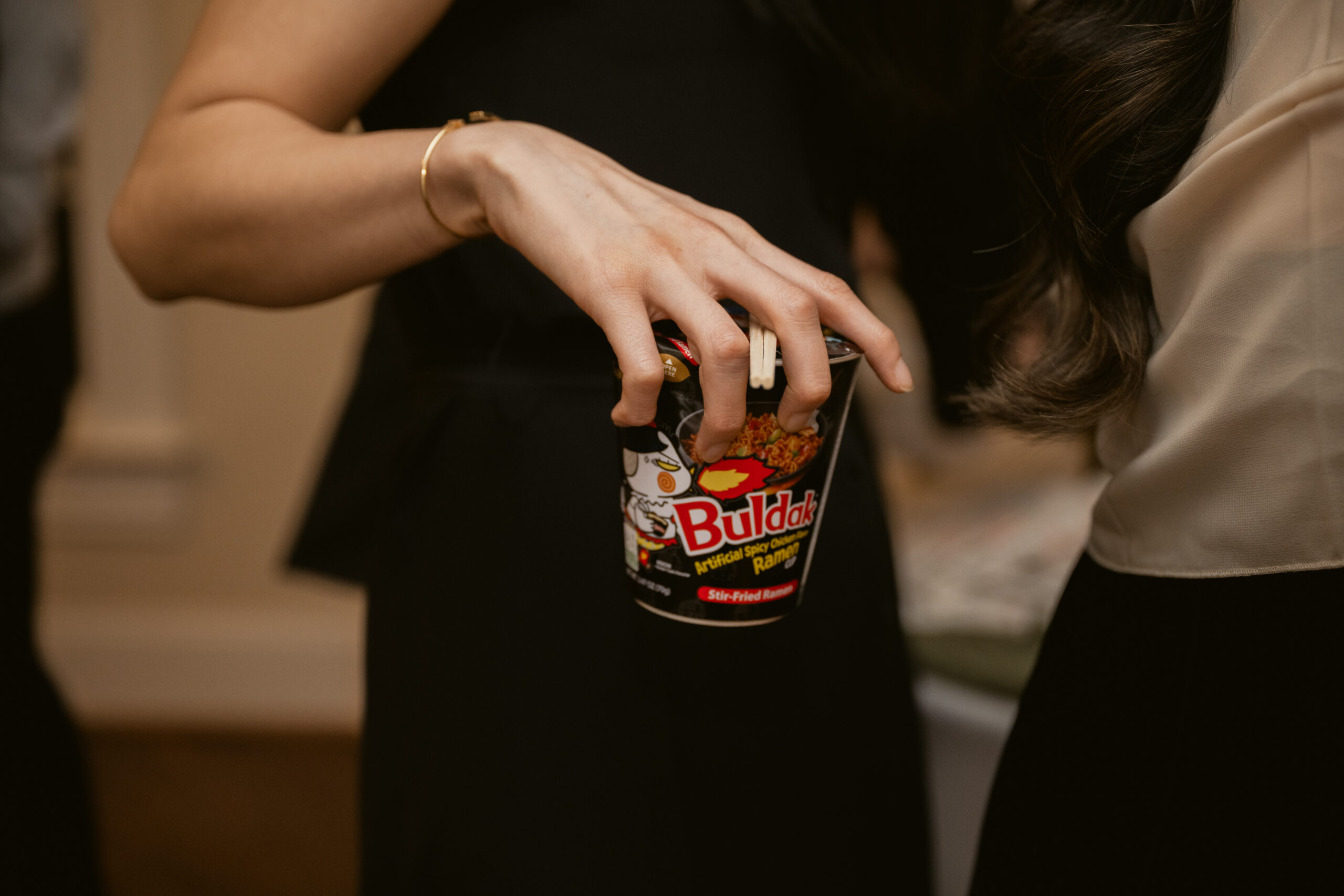 Close-up of a wedding guest holding a cup of Buldak instant ramen with chopsticks.