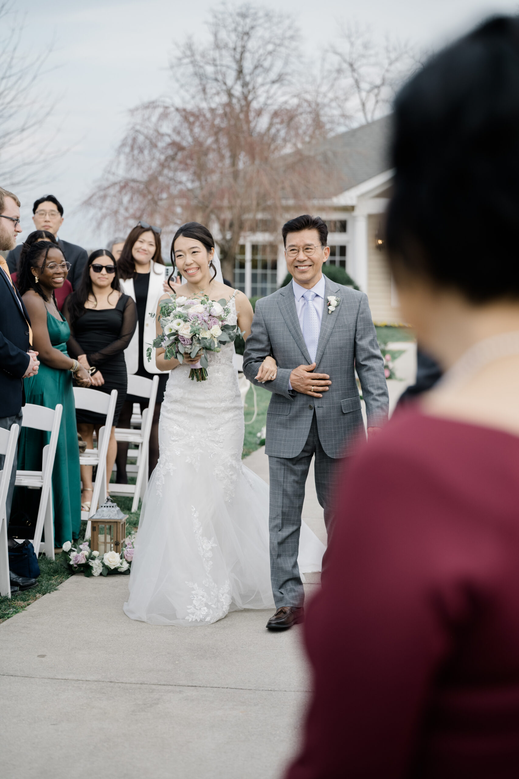 Bride smiling as she walks down the aisle arm-in-arm with her father during the outdoor wedding ceremony at Springfield Manor, surrounded by standing guests and floral aisle decor.