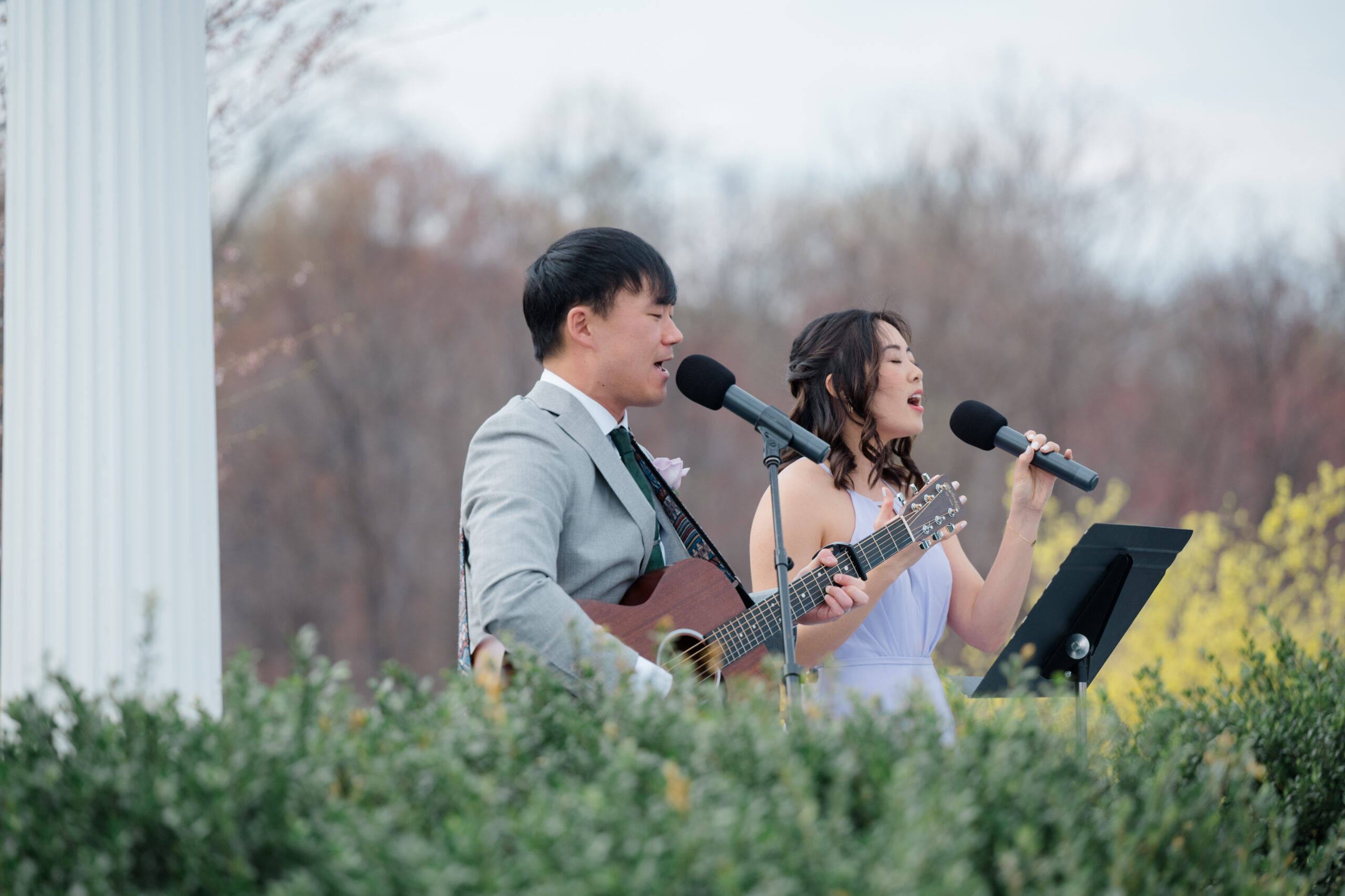 Bride and groom worship with eyes closed and hands raised during their outdoor wedding ceremony, surrounded by soft greenery and spring florals.
