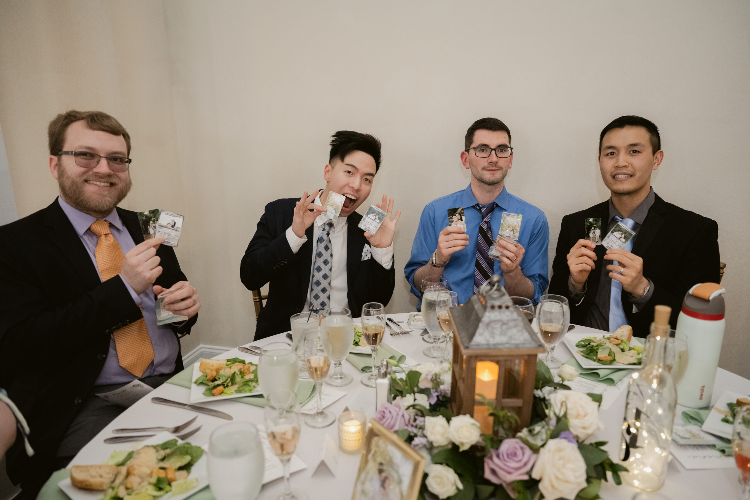 Group of four wedding guests holding up personalized cards featuring the couple at their dinner table.