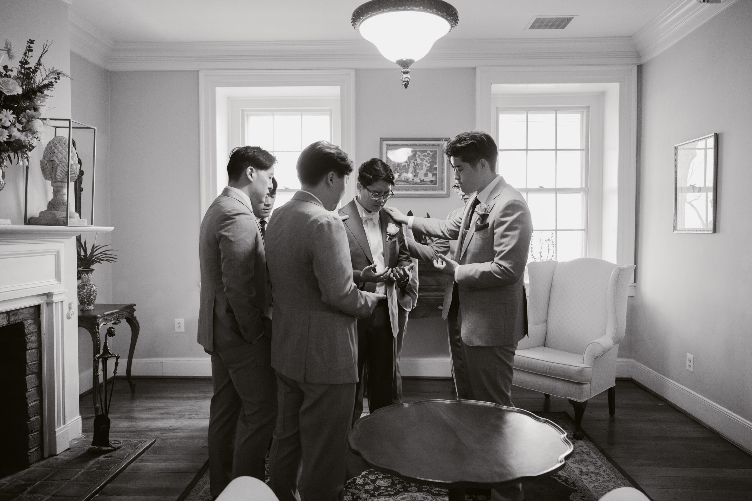 Groom and groomsmen sharing a quiet moment of prayer and support before the wedding ceremony at Springfield Manor, captured in black and white.