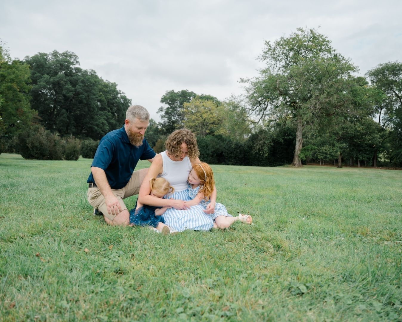 Family sitting together in the grass, cuddling and laughing during their motherhood session.