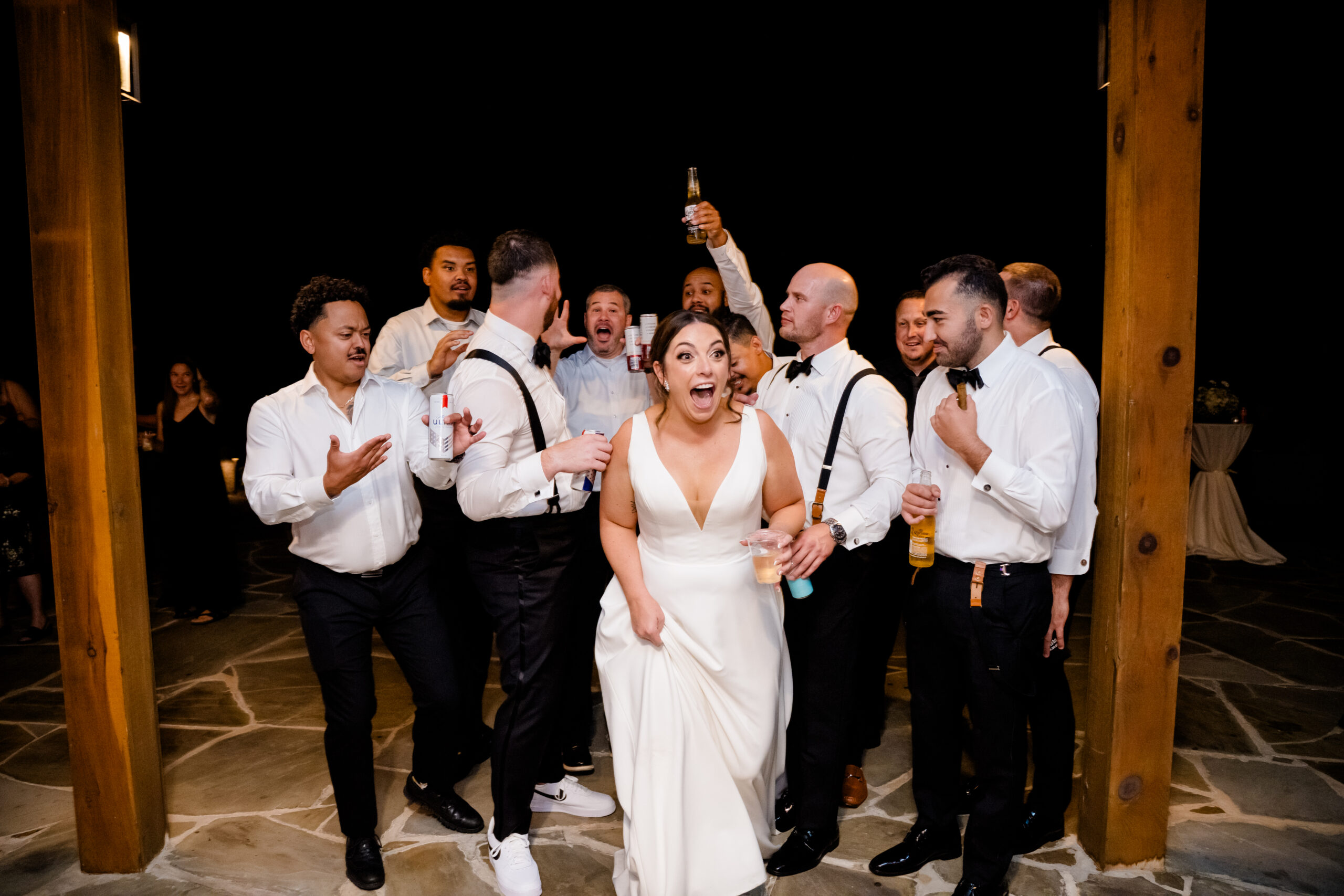 Bride surrounded by friends and wedding party laughing during a joyful nighttime celebration