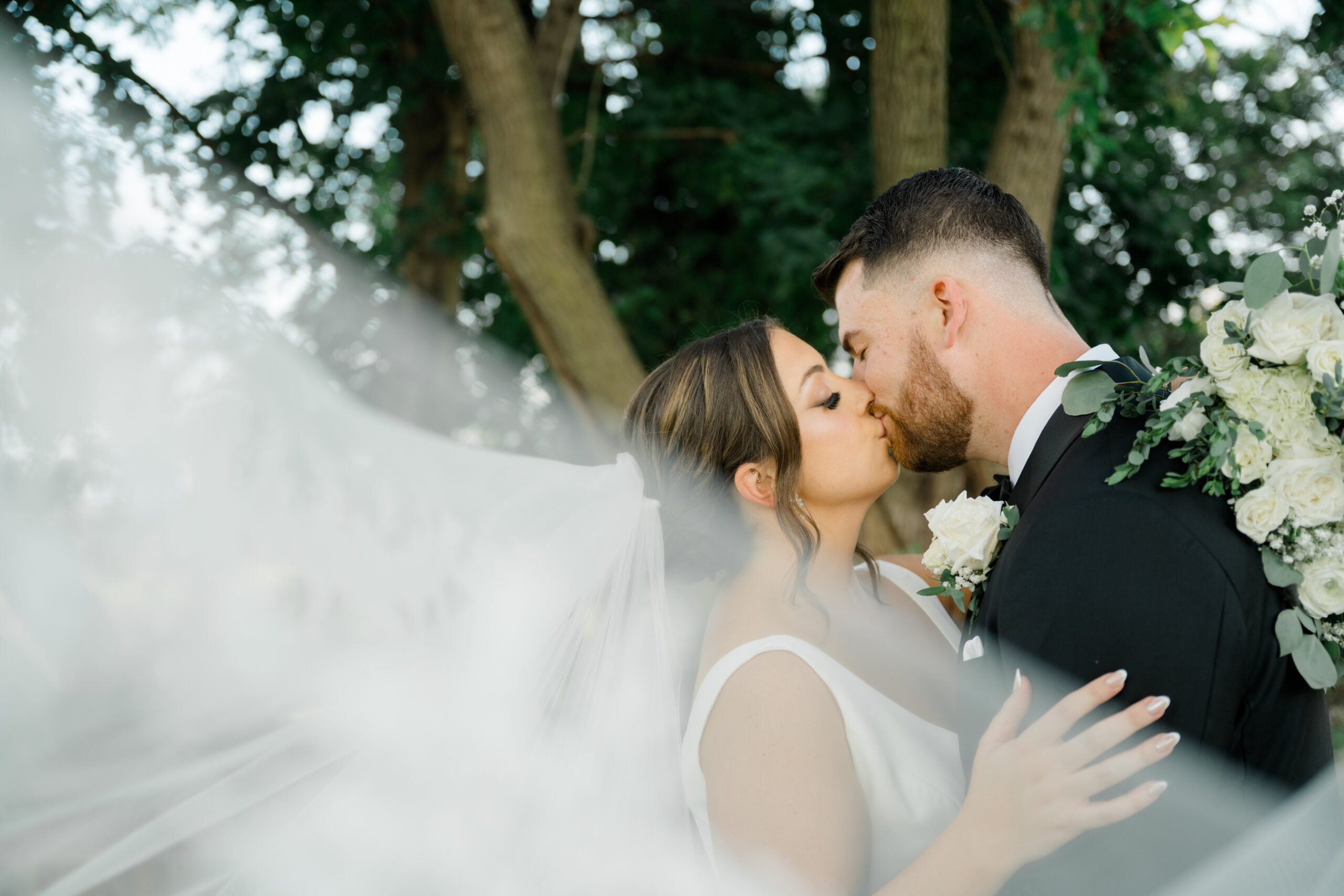 Bride and groom kissing softly during portraits as the bride’s veil flows between them