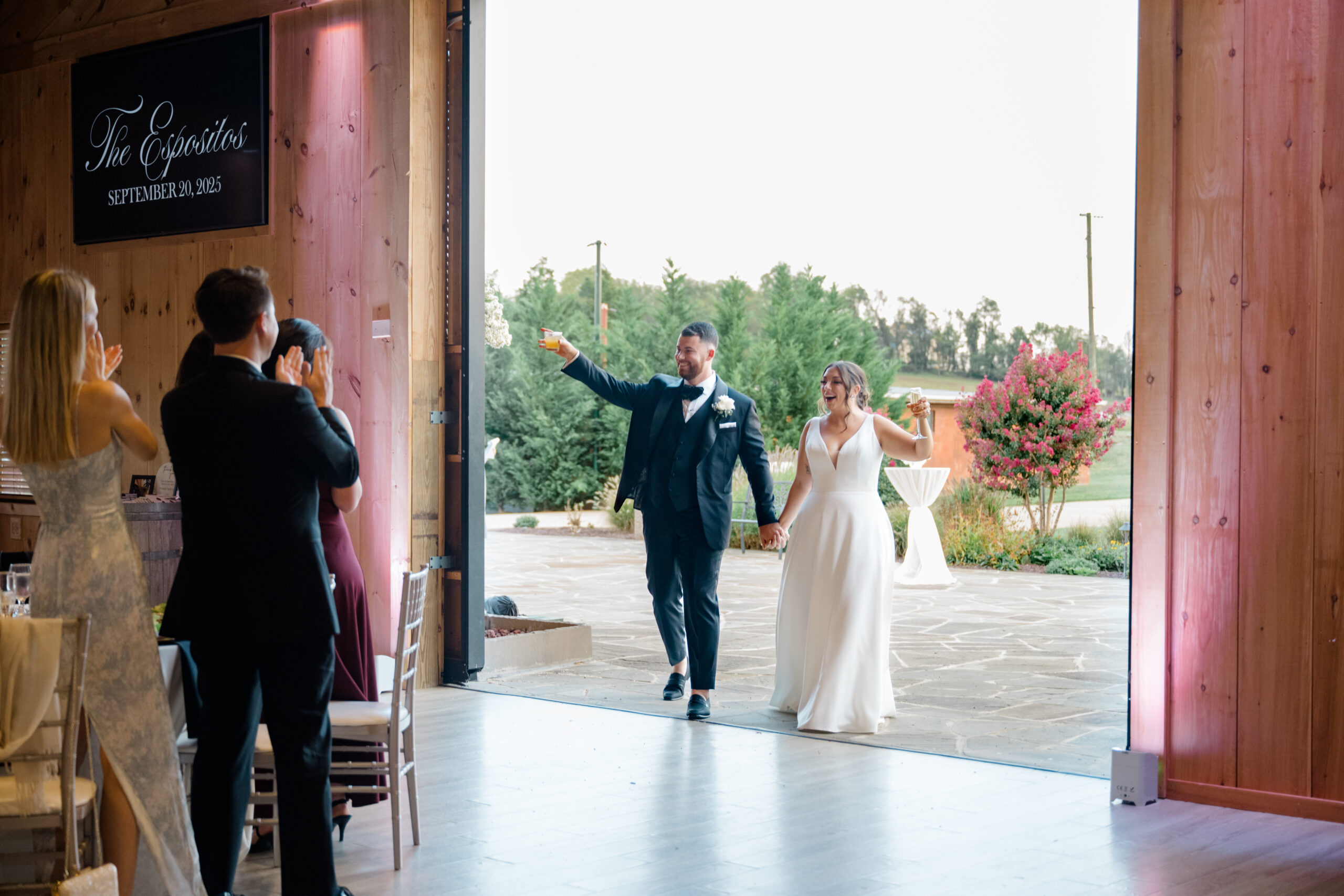 Bride and groom entering the reception hand in hand while raising a toast to their guests