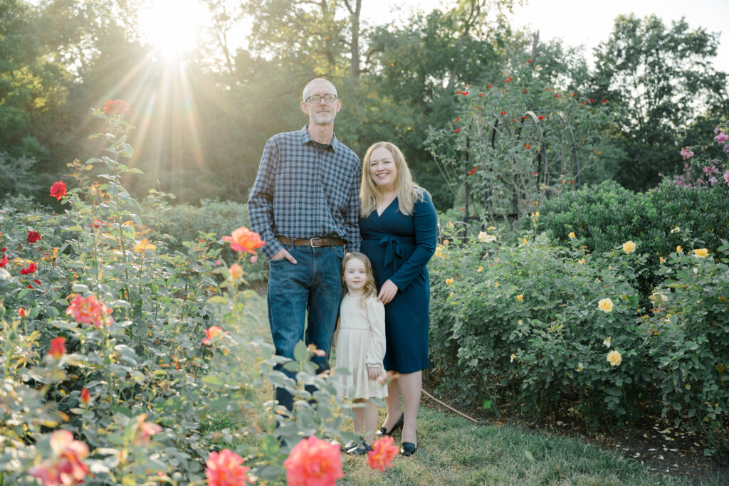 Family standing together among blooming roses during a golden hour mini session at the Bon Air Rose Garden in September.