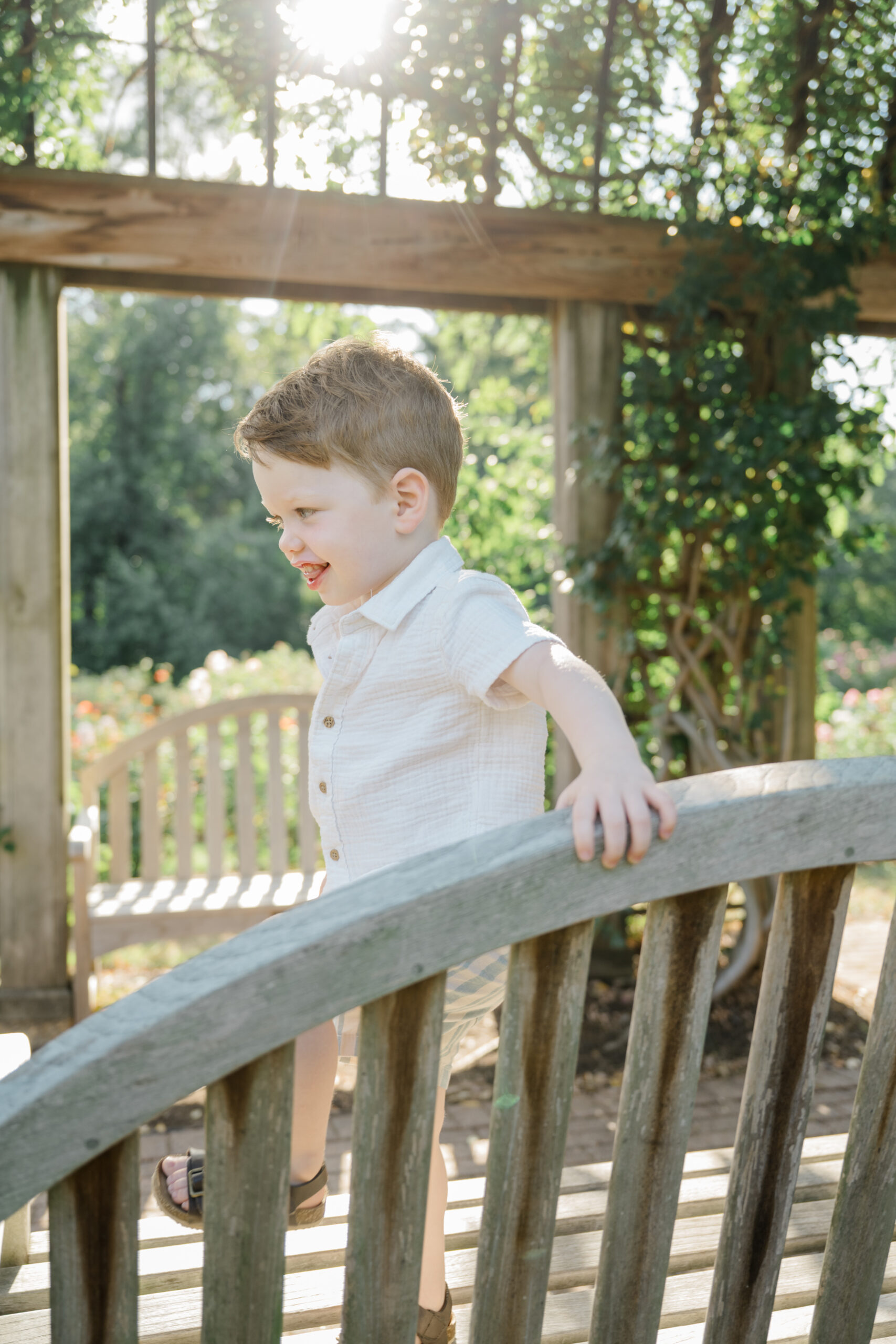 Outdoor spring photo of a toddler standing on a wooden bridge surrounded by greenery during a family session.