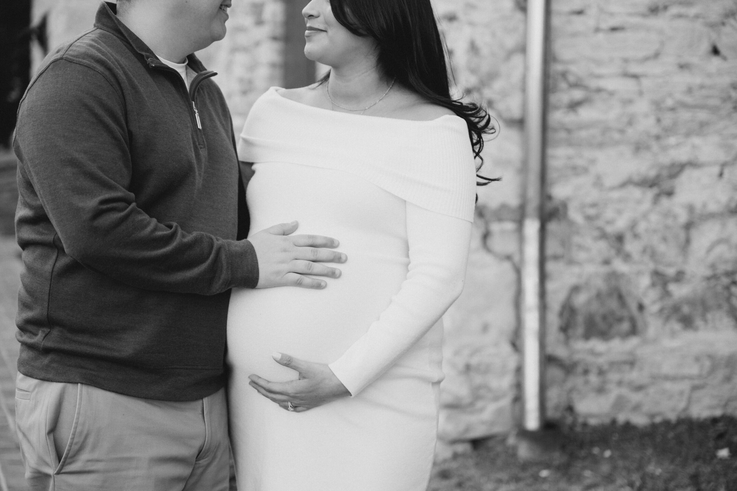Black and white winter maternity photo of an expecting couple standing close together, with hands resting on the baby bump during an outdoor session.