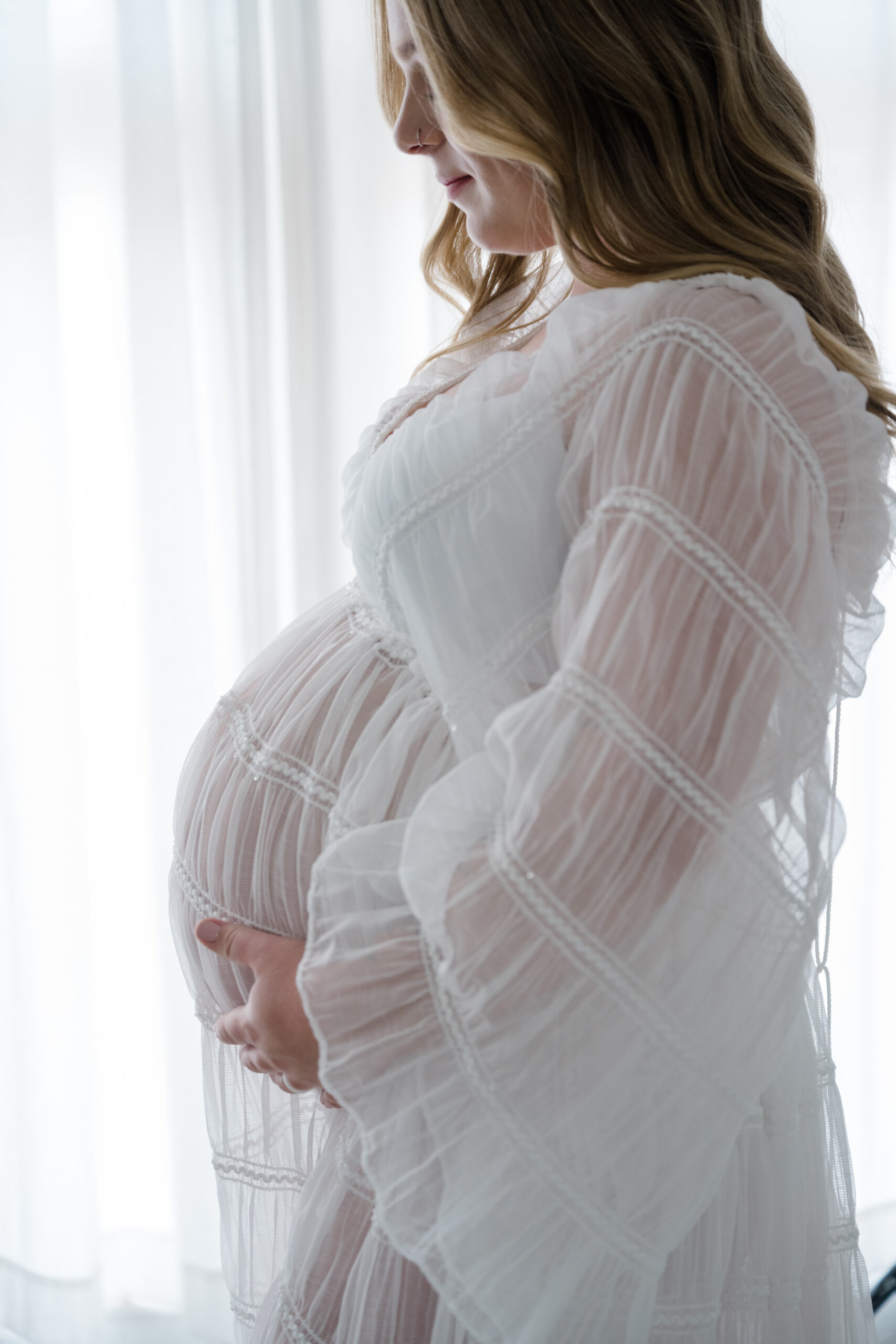 Close up studio maternity portrait of an expecting mother gently holding her baby bump in soft natural light.
