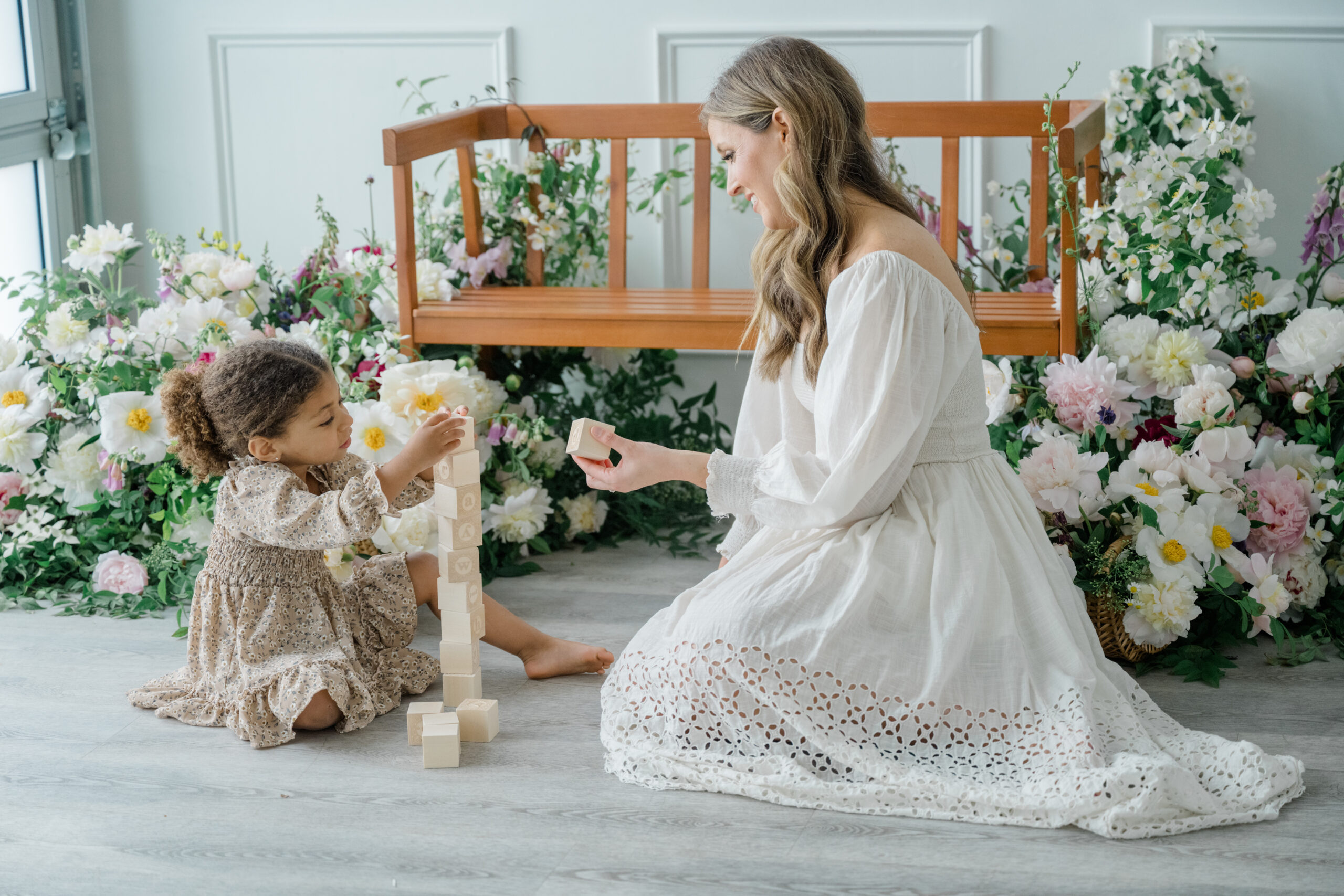 Mother and toddler sitting on the studio floor, playing with wooden blocks in front of a floral backdrop during a motherhood session.