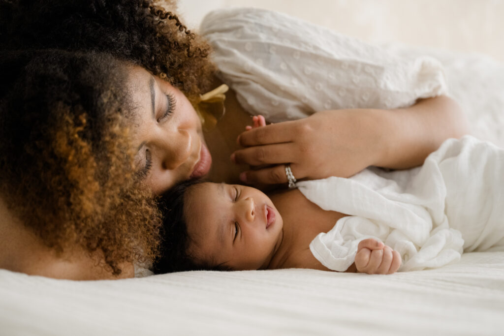 Mother lying beside her newborn, gently holding the baby close during a quiet in-home moment.
