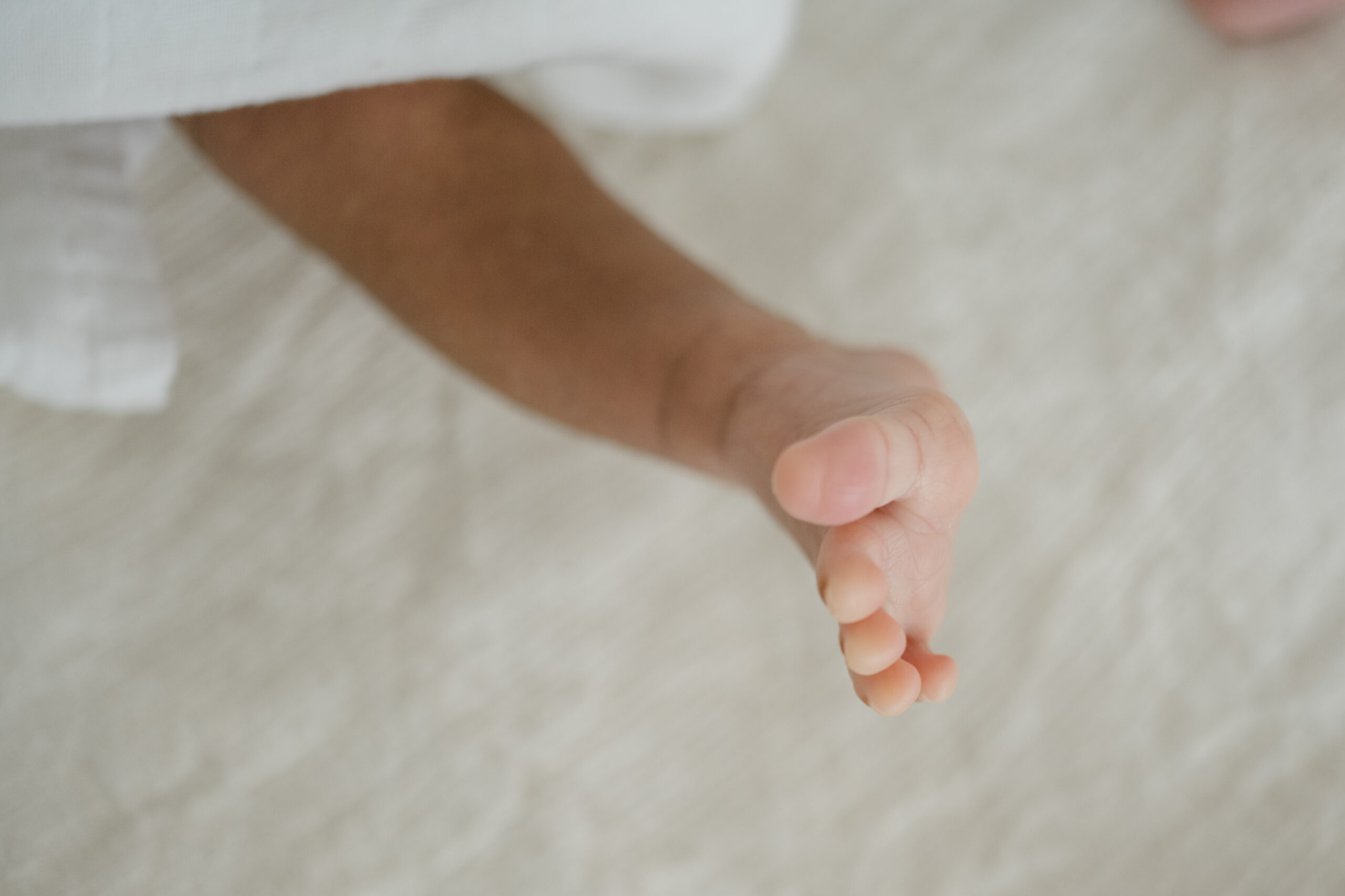 Close up detail photo of a newborn’s tiny foot resting on a soft neutral surface.