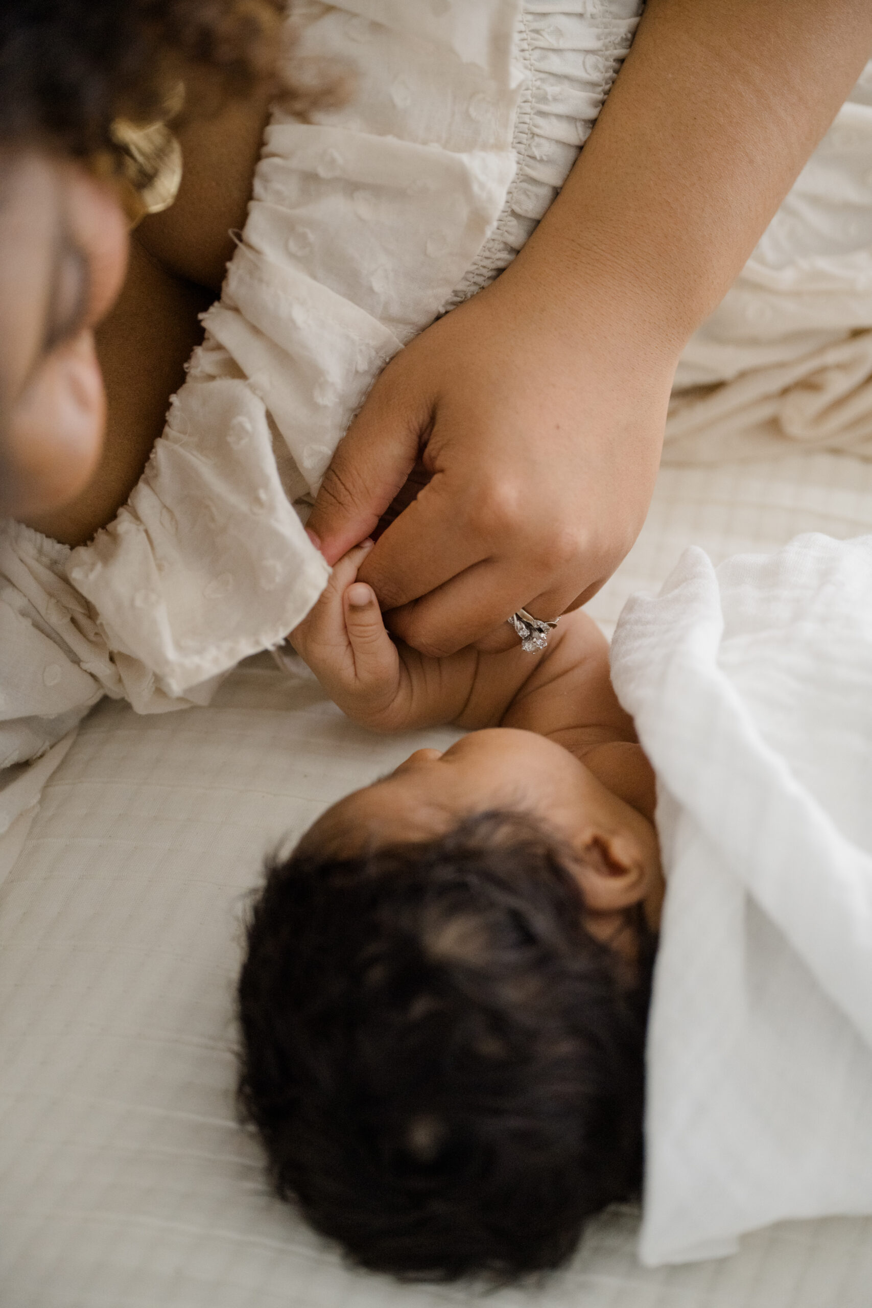 Close up newborn detail photo of a baby holding their mother’s finger while lying on a soft neutral bed.
