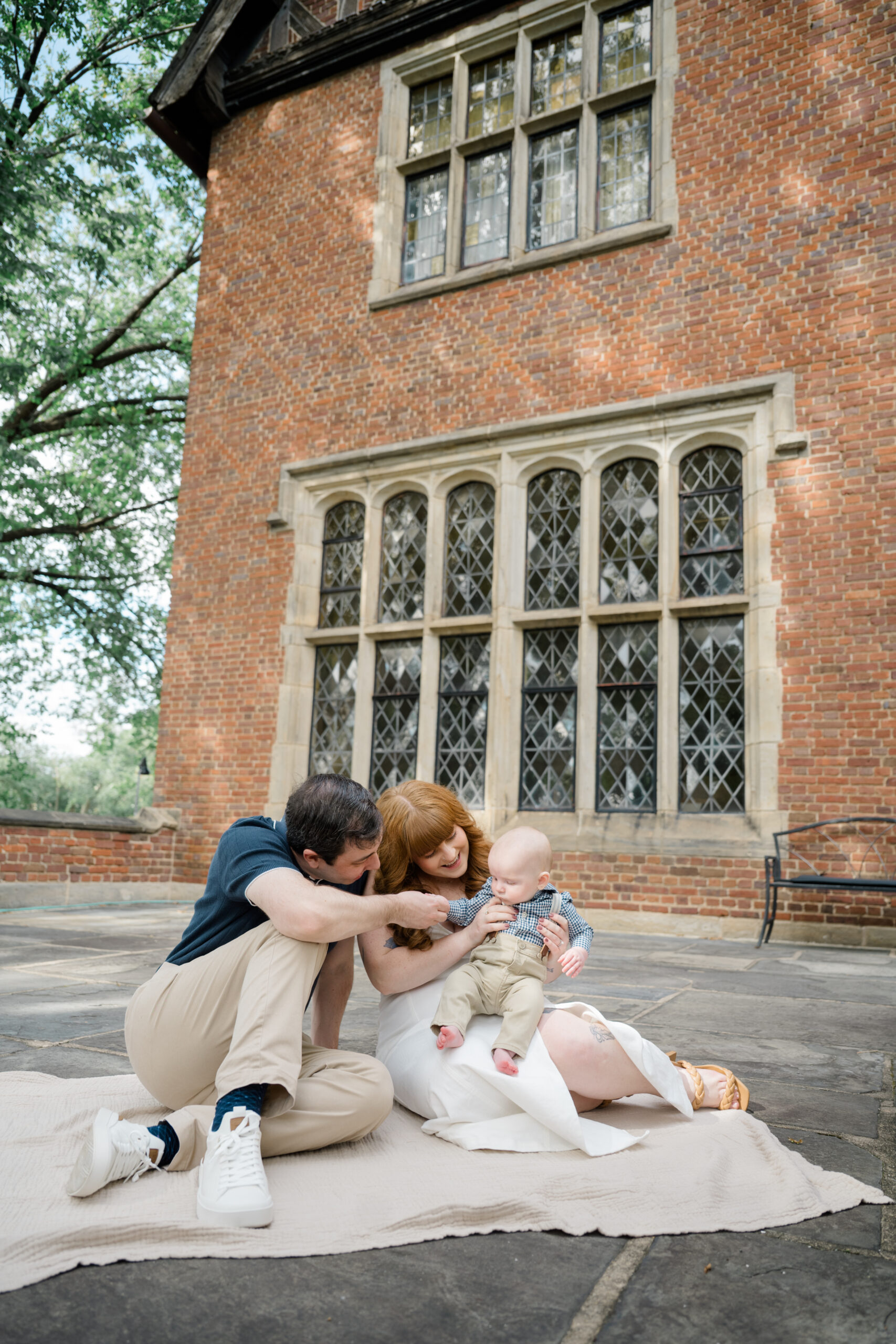 Family sitting together on a blanket in front of a historic brick building during an outdoor portrait session.
