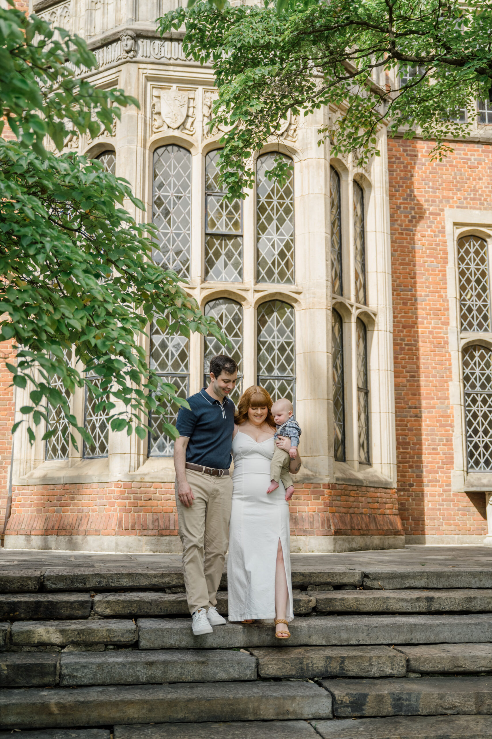Family walking down stone steps in front of a historic brick building with tall windows and greenery during a portrait session.