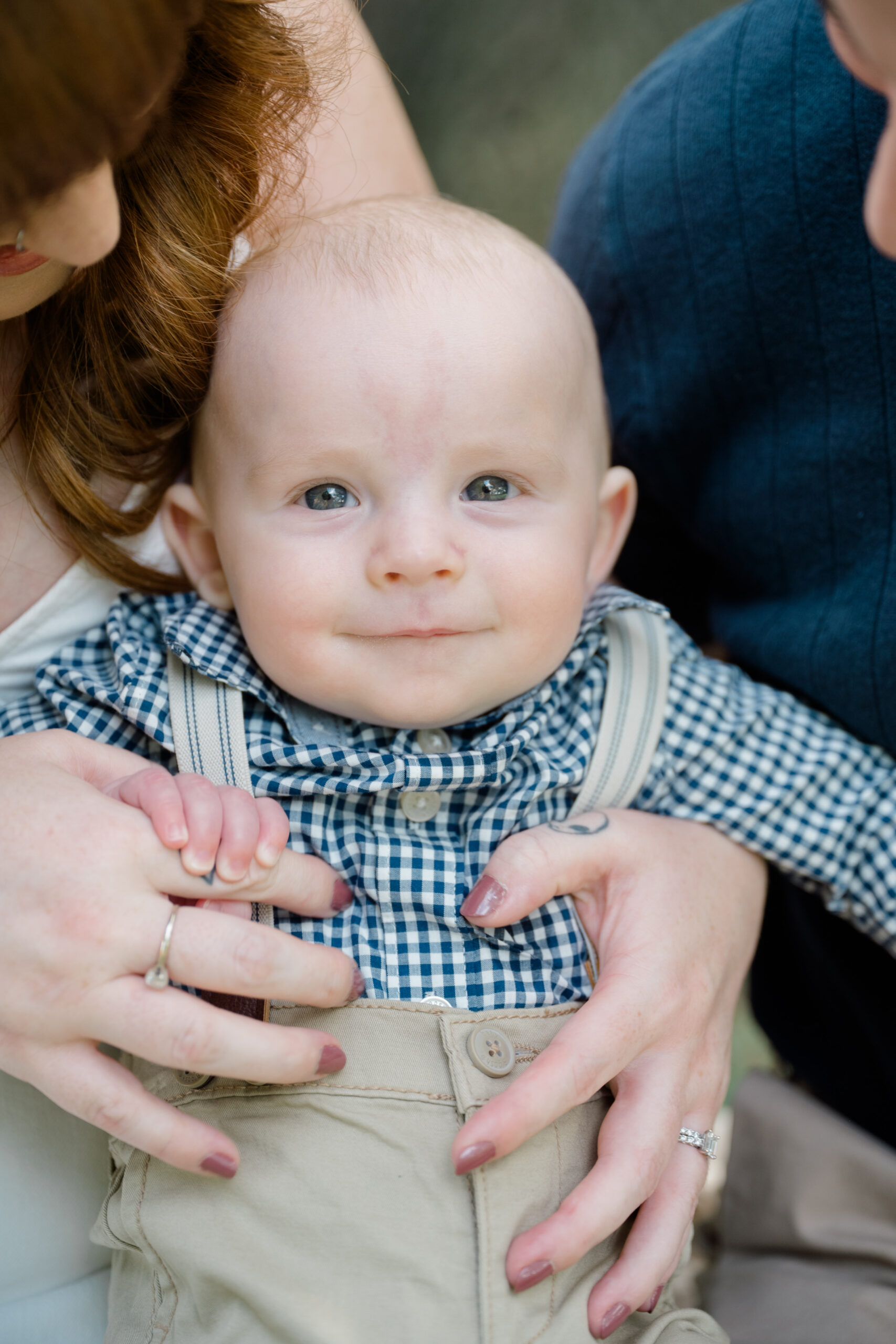 Close up portrait of a baby being held by parents, looking toward the camera during a family photo session.